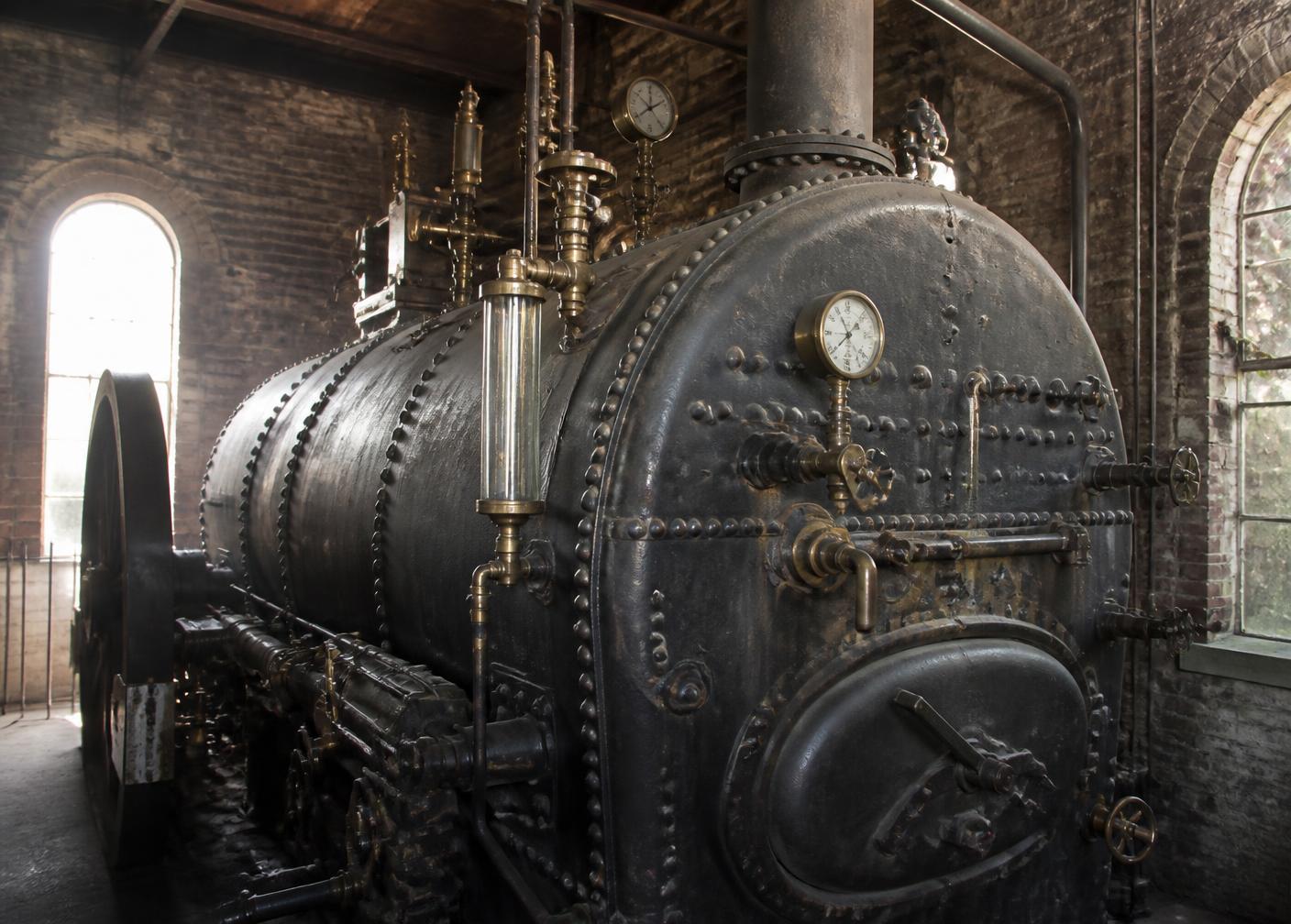 Riveted heritage steam boiler with brass fittings and gauges in a brick engine house